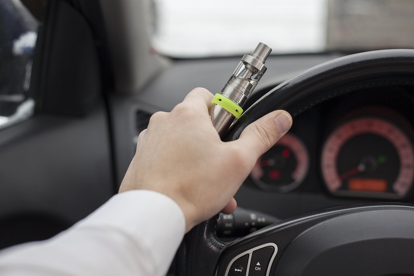 Hand eines Autofahrers hält gleichzeitig die E-Zigarette und das Lenkrad fest