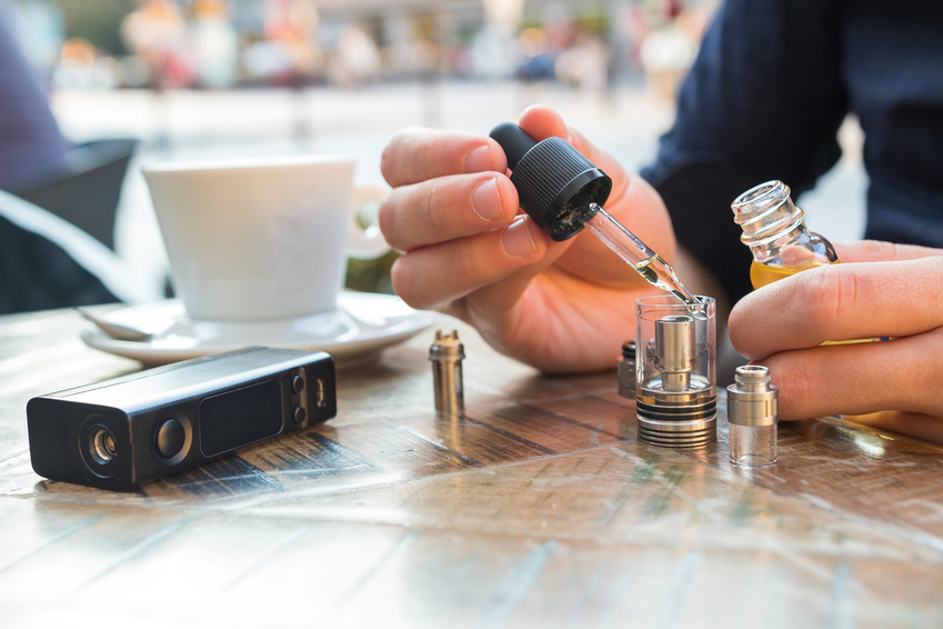 Mann befüllt den Tank seiner E-Zigarette mit Liquid, während er im Außenbereich eines Cafes ist