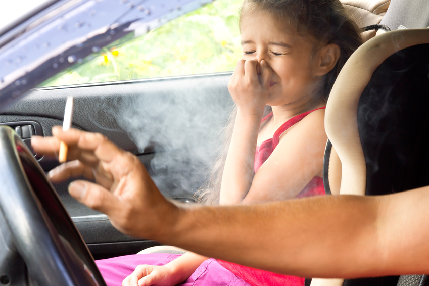 Person raucht im Auto mit Kind, das Kind hält sich die Nase zu
