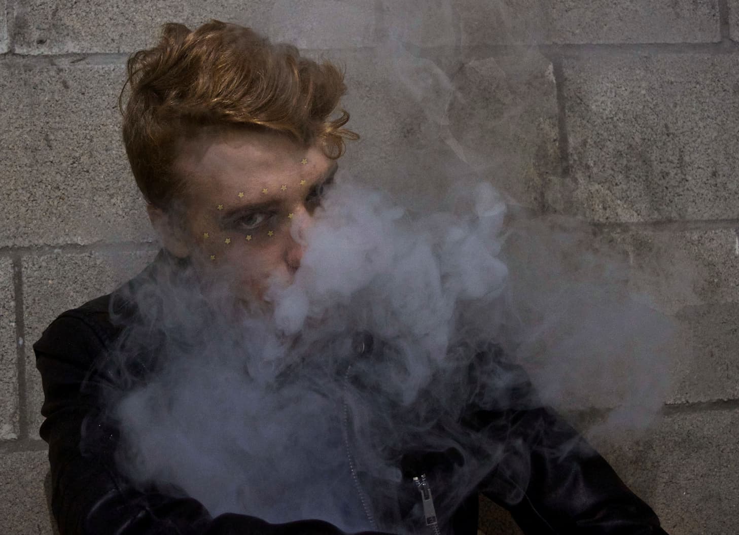 Junger Mann steht mit Dampf vor dem Gesicht an einer Mauer