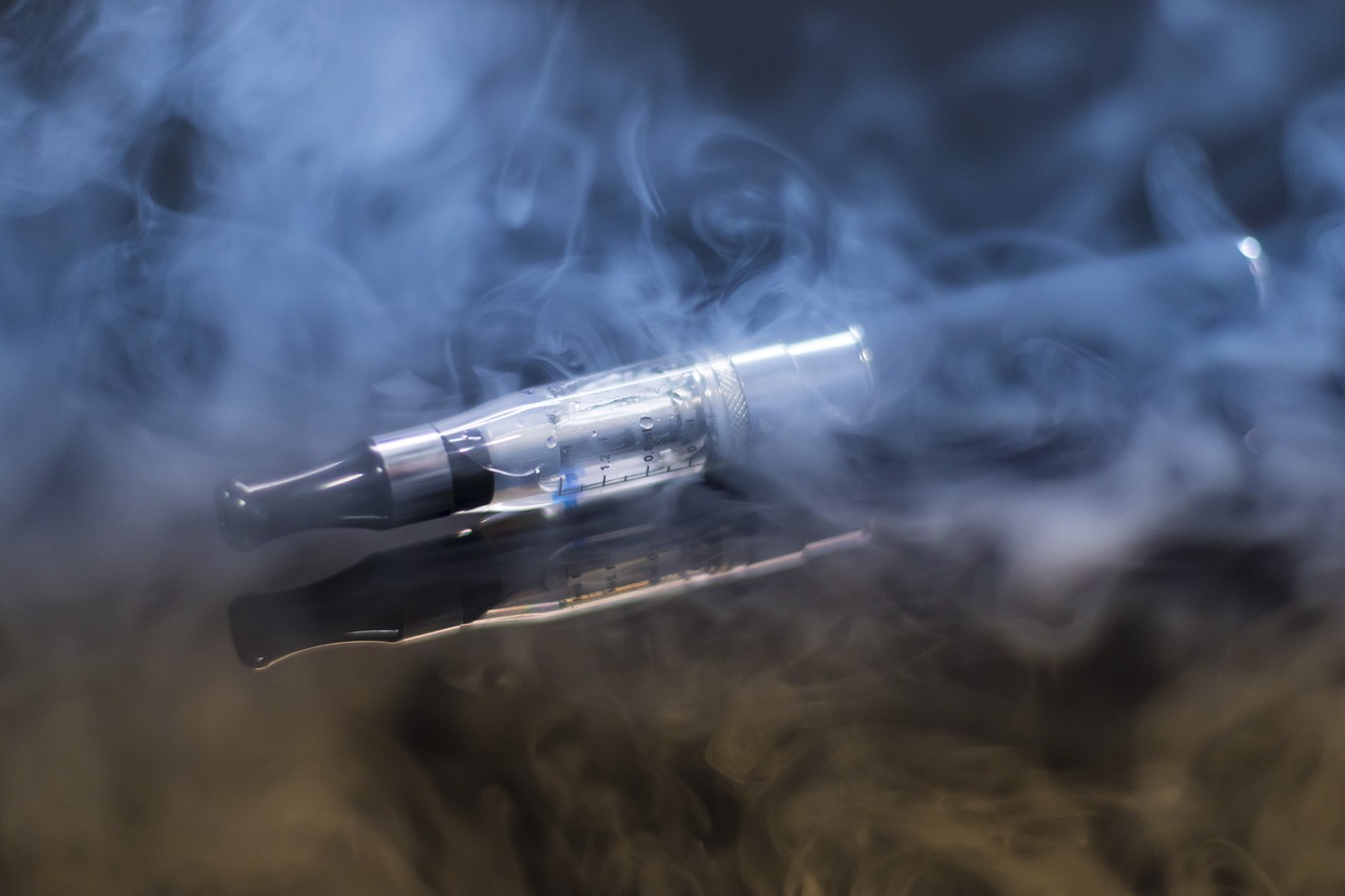 Silber-schwarze E-Zigarette liegt auf schwarzer Oberfläche in Dampf
