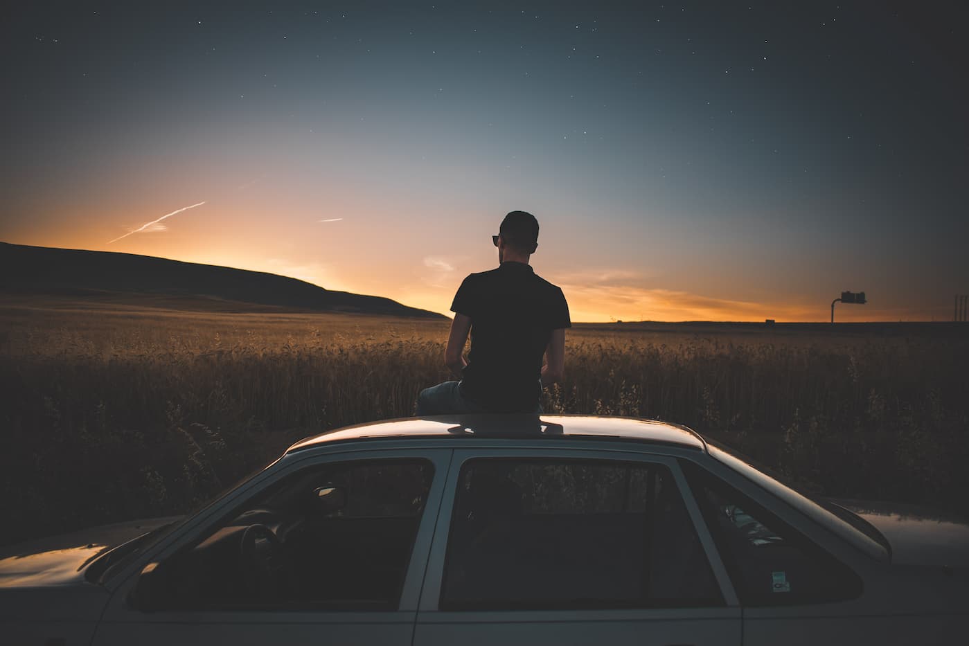 Mann sitzt auf Autodach und schaut auf den Horizont